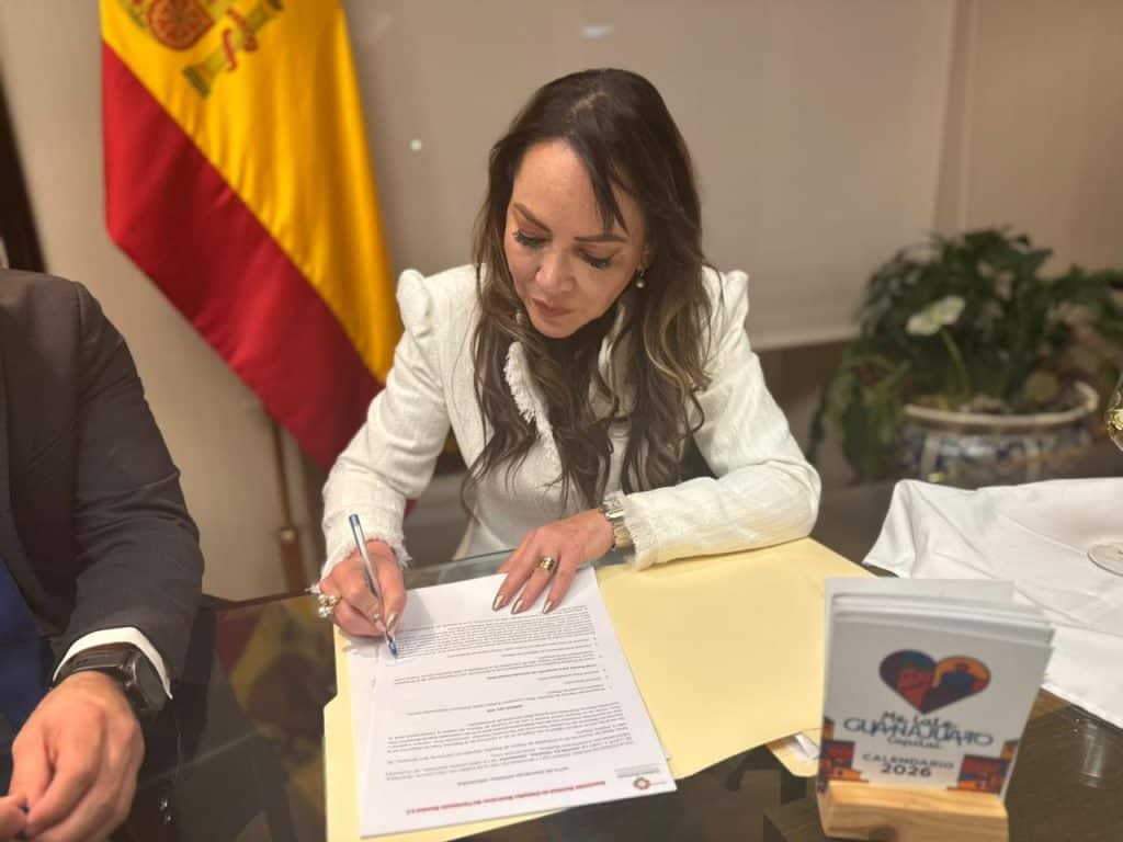 Firma de acuerdo oficial por una mujer en un evento formal con bandera de España al fondo.